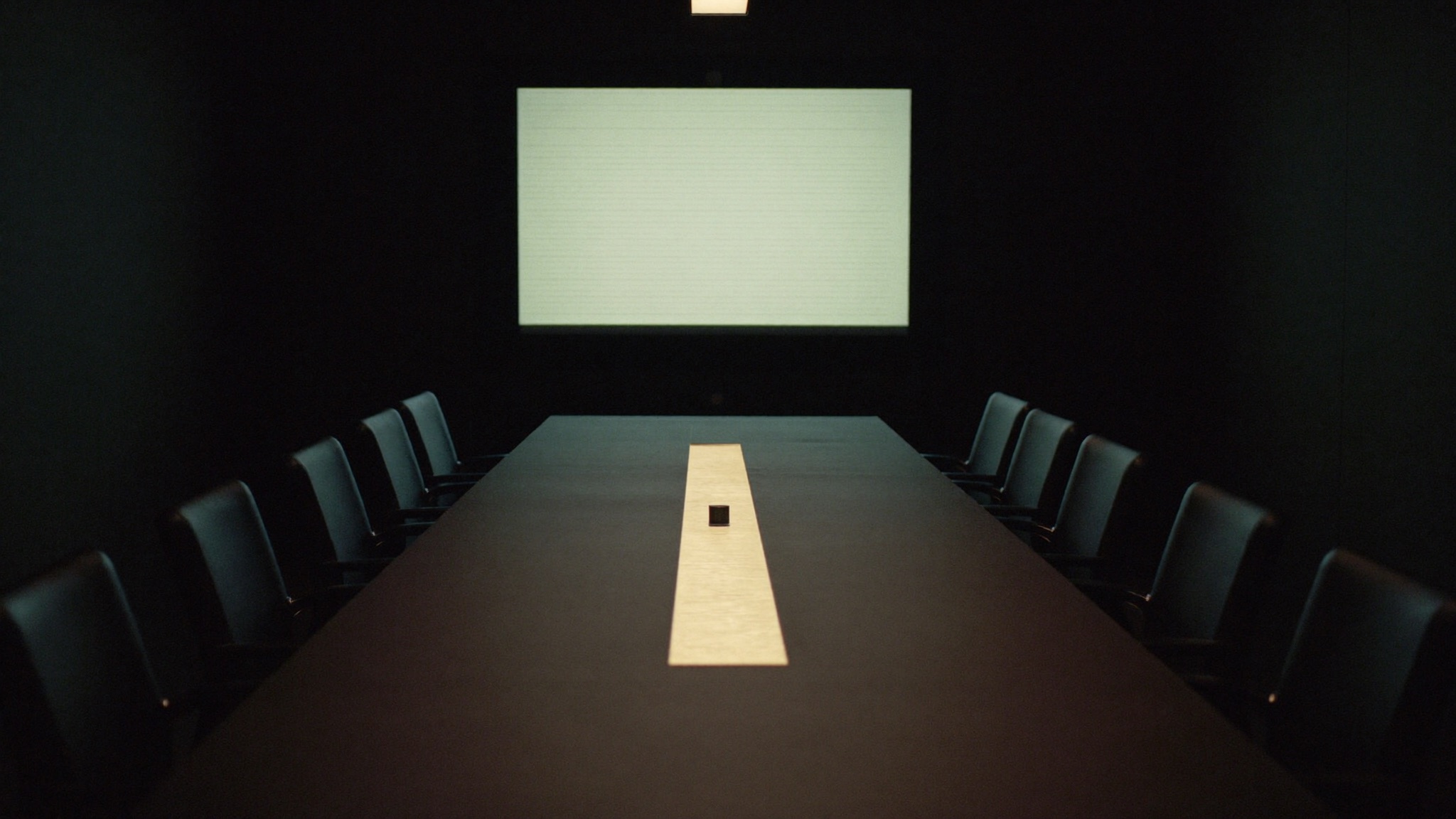 A dark conference room with a glowing wall screen