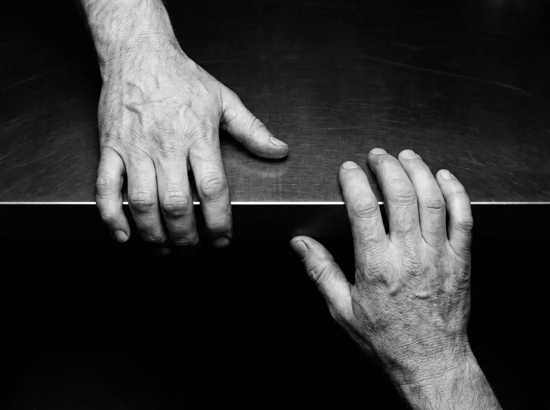 Two hands resting either side of a thin seam of light on a black workbench