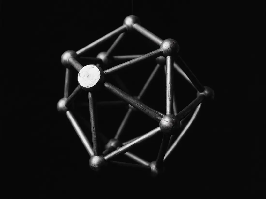 A machined metal node lattice suspended against black, lit from one side