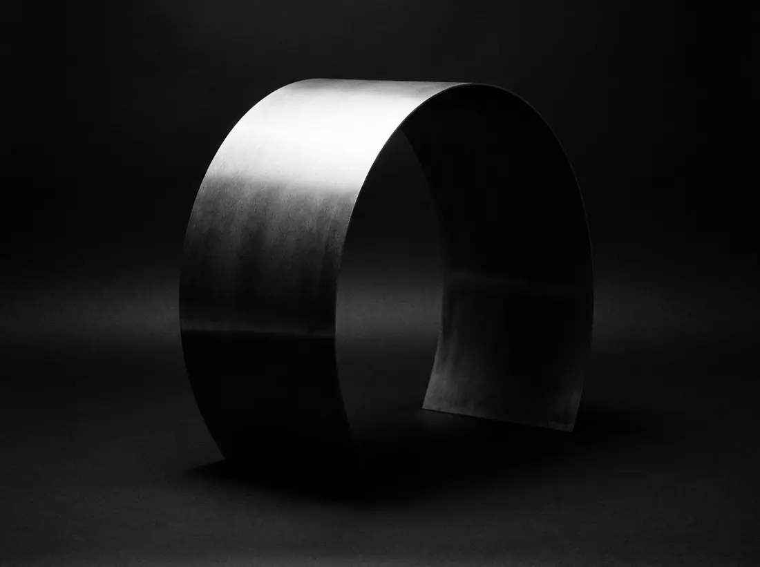 A large curved sheet of brushed black metal catching a single sweep of light