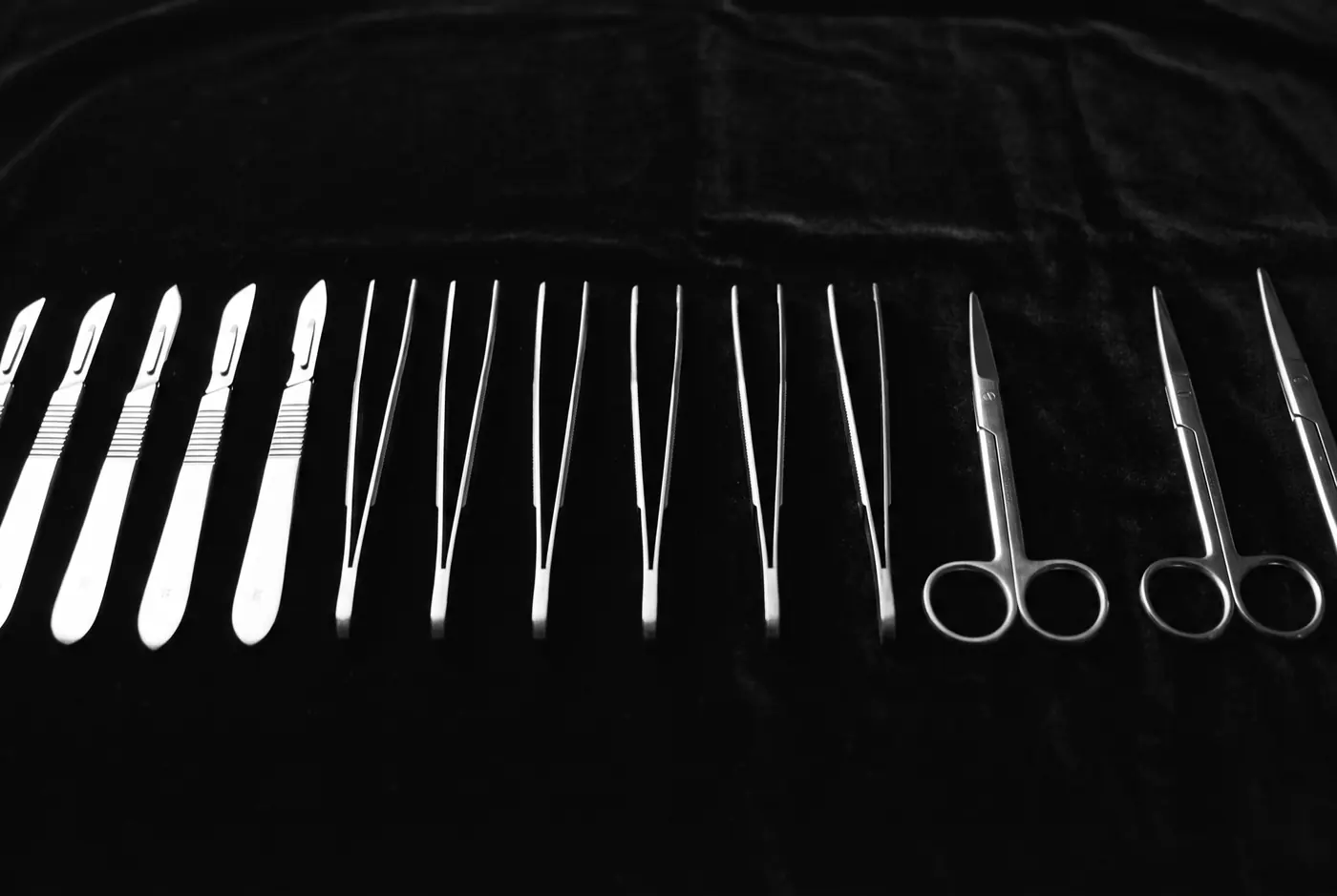 A row of polished surgical instruments laid out in parallel on black cloth