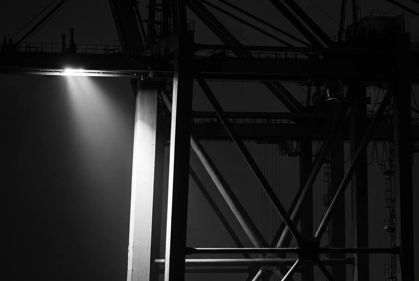 Gantry cranes and container stacks at a port at night under a single floodlight